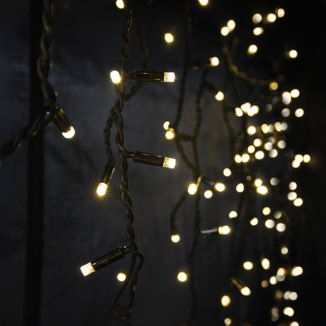 Close-up of the LYYT 180 LED Outdoor Icicle String Light - Warm White, glowing elegantly against a dark background. These energy-efficient LEDs are arranged in vertical strands, emanating a soft and warm illumination that creates a cozy and festive atmosphere, ideal for outdoor use.