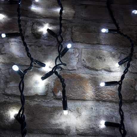 LYYT 180 LED outdoor icicle string lights in cool white with black rubber cable, shown lit against a rustic stone brick wall.