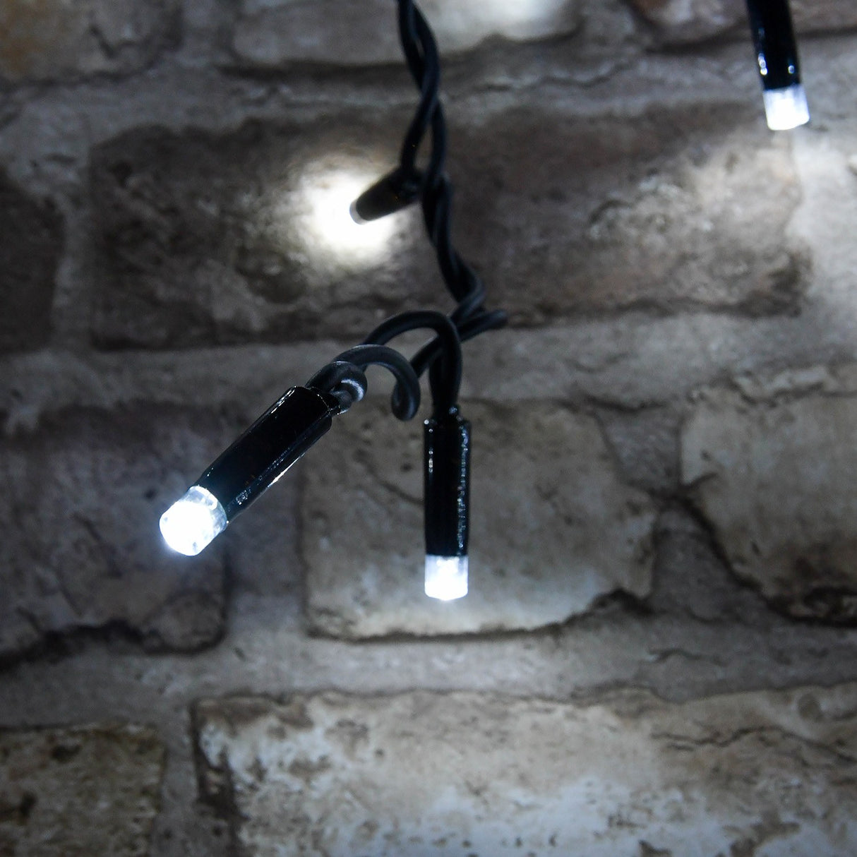 Close-up of LYYT LED icicle string lights by AVSL, showing cool white concave LED tips on black rubber cable against a rustic stone brick wall.