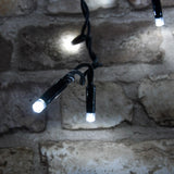 Close-up of LYYT LED icicle string lights by AVSL, showing cool white concave LED tips on black rubber cable against a rustic stone brick wall.