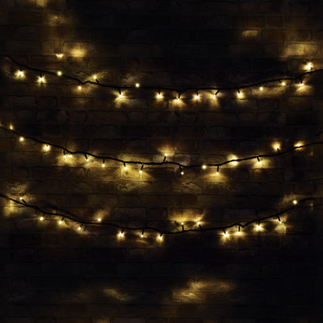 The LYYT 90 LED Heavy Duty LED String Lights With Controller, stretching 11 meters, emit a warm white glow as they hang in rows against a dark brick wall, crafting a cozy and festive atmosphere ideal for outdoor use while being delightfully energy efficient.