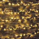 LYYT 180 LED heavy duty string lights in warm white draped in horizontal runs across an exposed brick wall, glowing softly on black cable.