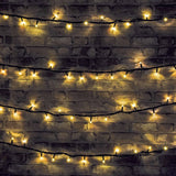LYYT warm white LED festoon string lights draped in four rows across a dark brick wall on black cable, glowing with a soft amber tone.