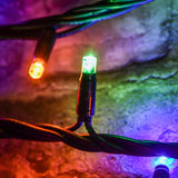 Close-up of a LYYT RGBA LED string light showing green and amber concave bulbs on heavy-duty black rubber cable against a textured stone surface.