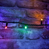 LYYT HD180S-MC RGBA heavy duty festoon string lights close-up with red, green and amber LEDs on black rubber cable against a rustic brick wall.