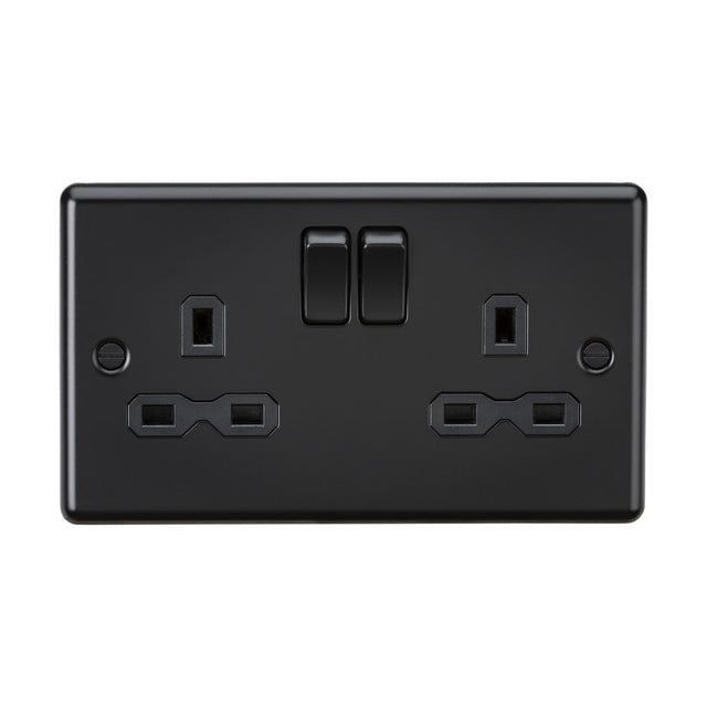 The 13A 2 Gang DP Switched Socket - Matt Black (Black Insert, Rounded Edge) features two three-pin outlets with switches above each, offering a premium finish that enhances contemporary spaces. Set against a pristine white background, it blends style and functionality seamlessly.