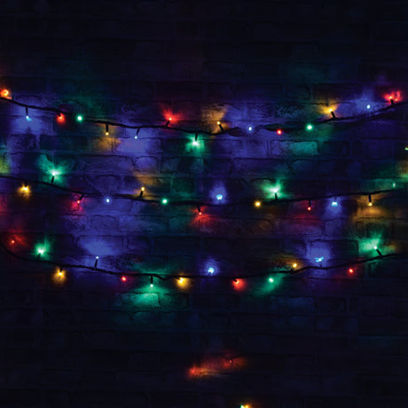 The LYYT 180 LED Heavy Duty LED String Lights With Controller, stretching 20 meters long and featuring a robust black cable, are elegantly draped against a dark brick wall. These lights illuminate in radiant red, green, blue, and amber shades, offering an energy-efficient festive and warm atmosphere.