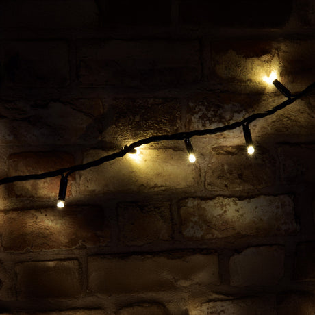 The LYYT 100 LED Outdoor Connectable Icicle String Lights, spanning 8 meters in warm white, drape against a rustic brick wall, warmly illuminating the scene. These IP44-rated, energy-efficient LEDs create a cozy ambiance perfect for any evening gathering.