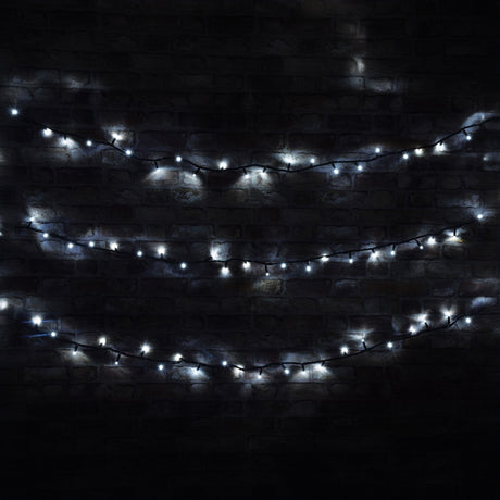 The LYYT 100 LED Outdoor Connectable Icicle String Lights, with their cool white glow, are arranged in three horizontal rows against a dark brick wall, creating a soft and ambient light in a dimly lit setting. These energy-efficient lights offer both charm and practicality for any evening gathering.