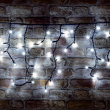 LYYT 100CONI-CW cool white LED icicle string lights with black cable in cascading drops, illuminated against an exposed brick wall.