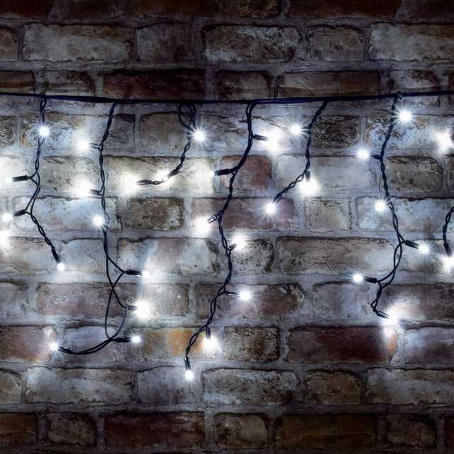 LYYT 100CONI-CW cool white LED icicle string lights with black cable in cascading drops, illuminated against an exposed brick wall.
