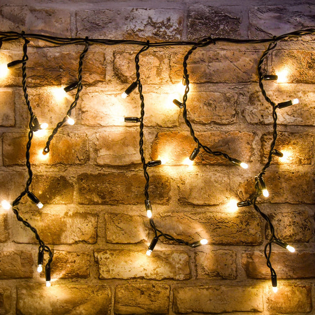 LYYT 100CONI-WW warm white icicle string lights with black cable draped along an exposed brick wall, showing varied drop lengths.