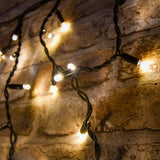 LYYT 100CONI-WW warm white connectable icicle lights by AVSL, illuminated on a rustic brick wall with black cable and hanging drops of varying lengths.