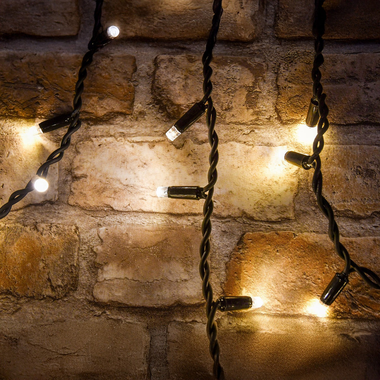 LYYT 100CONI-WW warm white icicle string lights with LED bulbs on black cable, draped against a rustic brick wall.