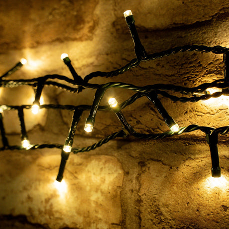 LYYT 200 LED string lights in warm white with dark green cable draped against a rustic stone wall, showing concave LED heads glowing softly.
