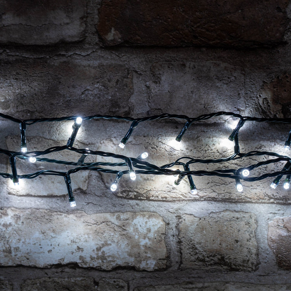 LYYT 200TS-CW cool white LED string lights on dark green cable, draped in rows across a rustic exposed brick wall.