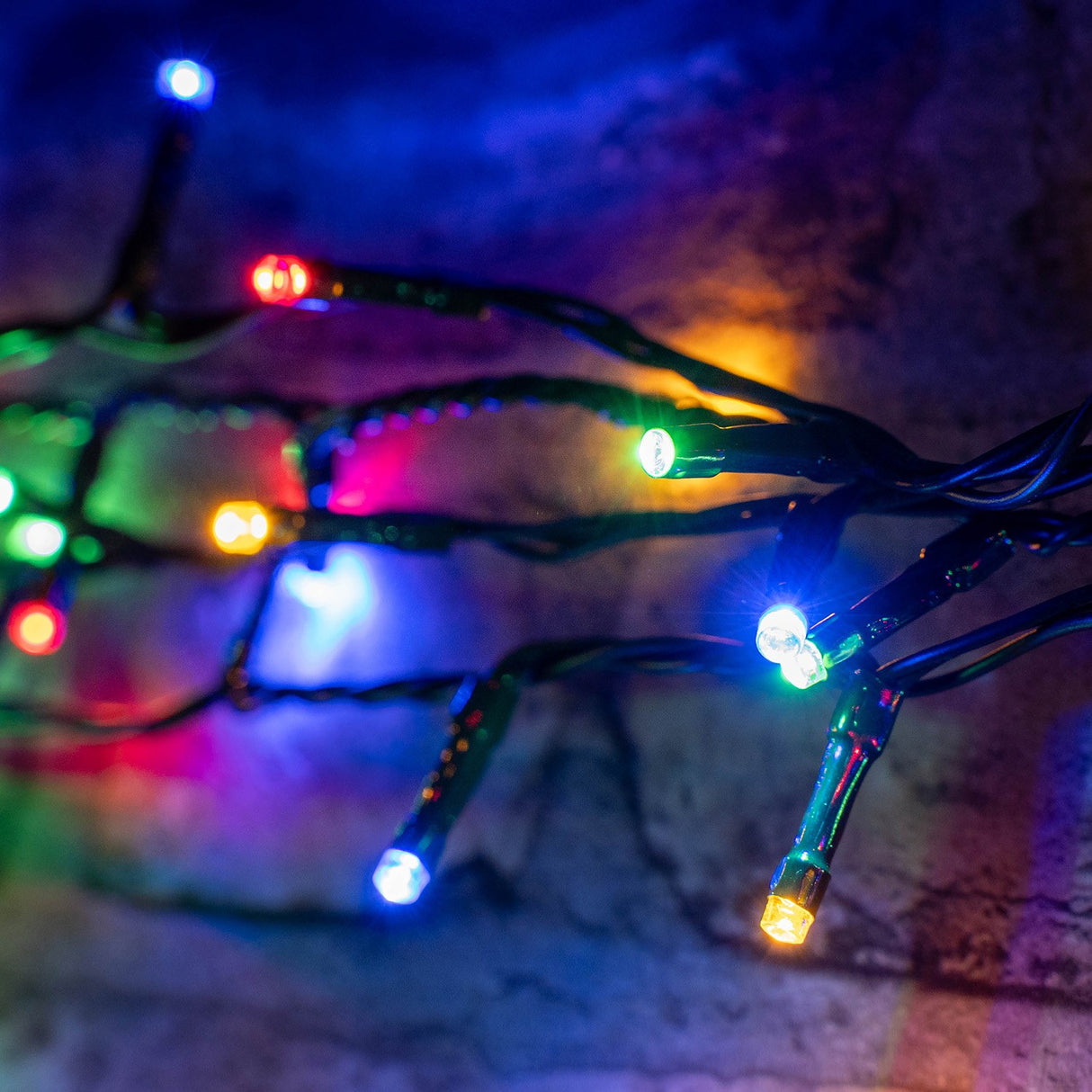 LYYT 200 LED RGBA string lights by AVSL draped on brickwork, showing red, green, blue and amber concave LEDs on dark green cable.