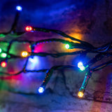 LYYT 200 LED RGBA string lights by AVSL draped on brickwork, showing red, green, blue and amber concave LEDs on dark green cable.