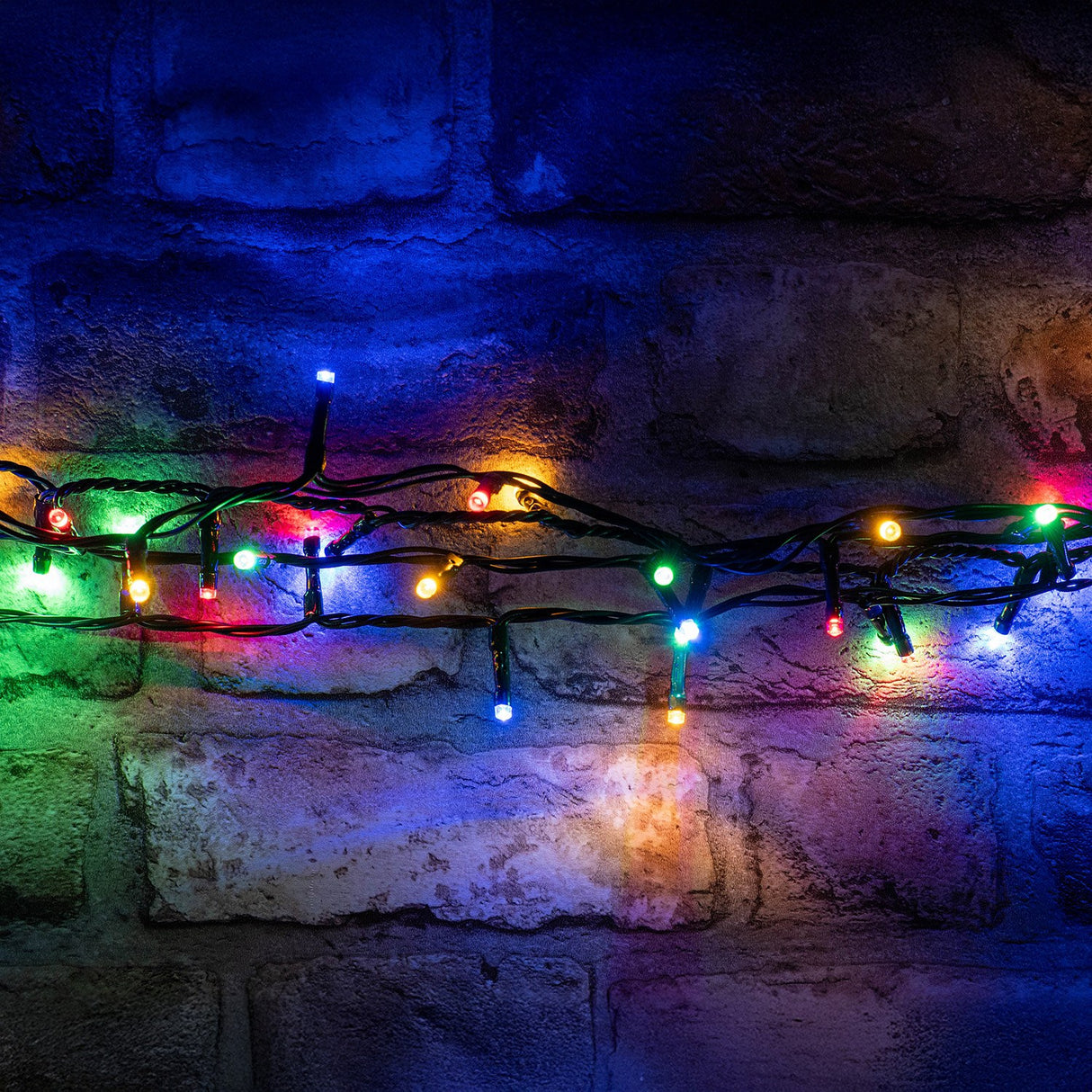 LYYT 200 LED RGBA string lights by AVSL draped on a rustic brick wall, showing red, green, blue and amber concave LEDs on dark green cable.