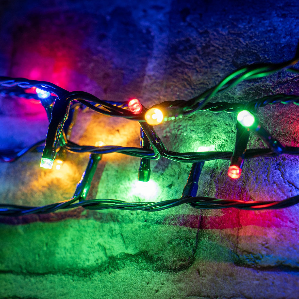 LYYT LED RGBA string lights illuminated in red, amber, green and blue along dark green cable wrapped against a textured brick wall.