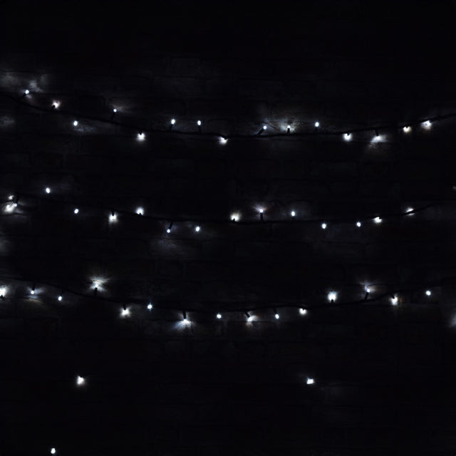 The LYYT 90 LED Heavy Duty String Lights with Controller, featuring 11 meters of cool white LEDs, are suspended in the darkness to form a pattern of glowing dots. They softly illuminate the surrounding area against the black background, providing an energy-efficient and festive ambiance ideal for outdoor use.