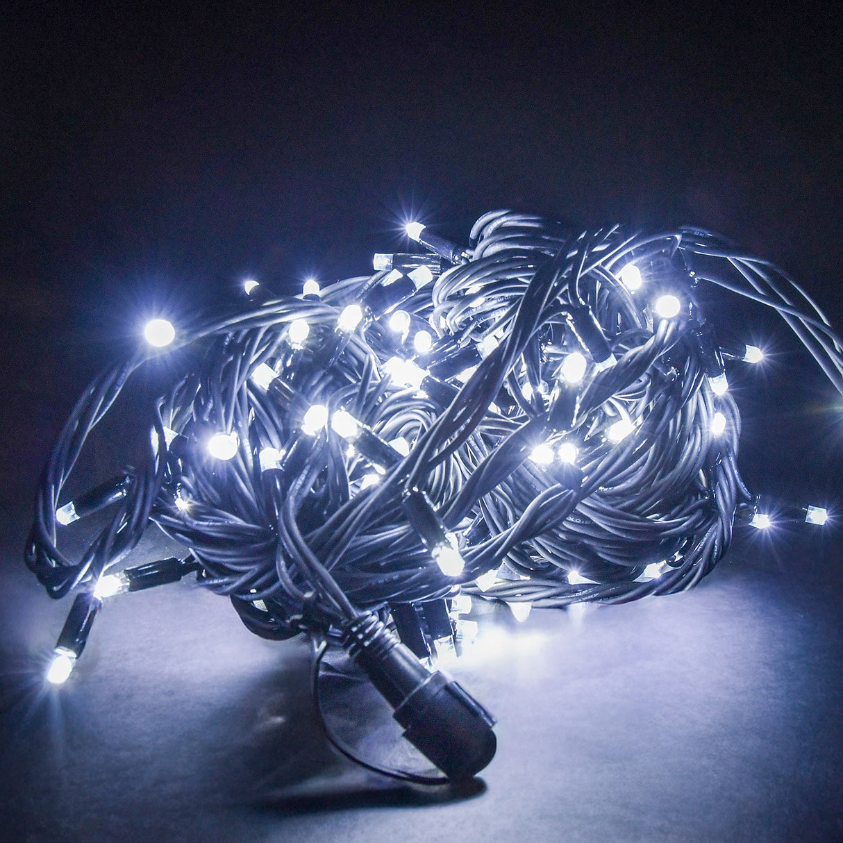 LYYT HD180C-WHT festoon lights coiled on a pale surface, cool white LEDs illuminated along heavy-duty black rubber cable against a dark background.