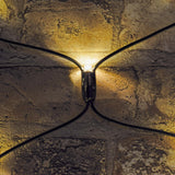 Close-up of a warm white LED on the LYYT 240 LED net light, showing the black rubber cable junction glowing against a textured stone wall.