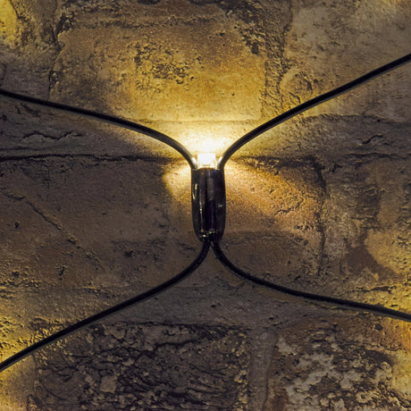 Close-up of a warm white LED on the LYYT 240 LED net light, showing the black rubber cable junction glowing against a textured stone wall.