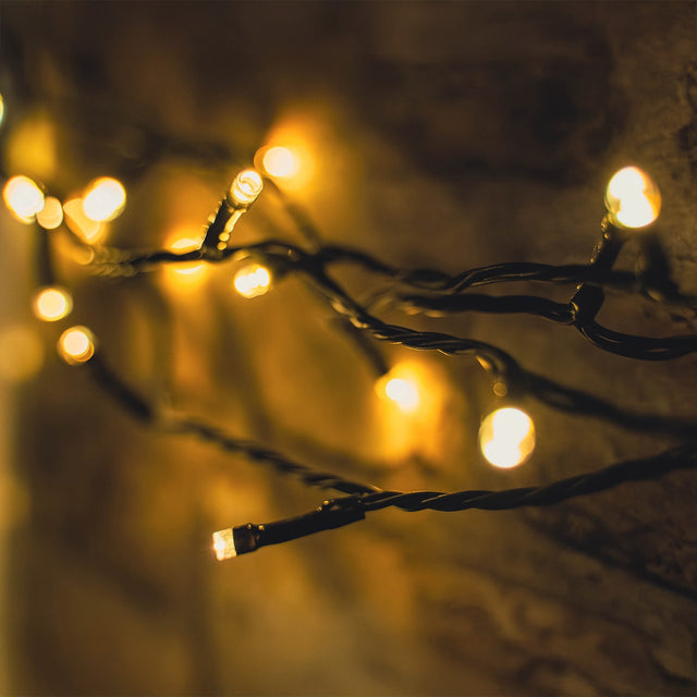 LYYT 120 LED Battery Topiary Ball Light string with warm white bulbs on a black cable, draped against a rustic brick wall.