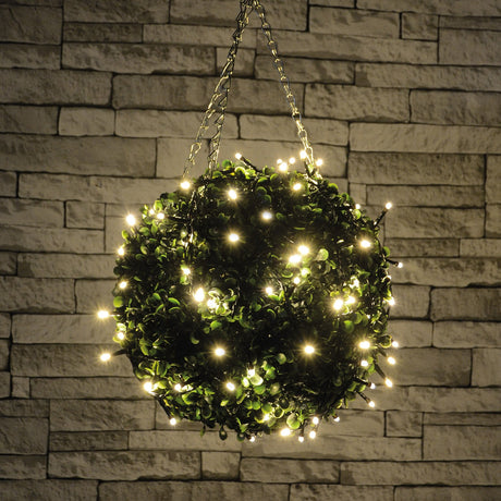 LYYT topiary ball light with 120 warm white LEDs wrapped around a green foliage sphere, hung by chains against a stone brick wall.