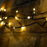 LYYT LED battery topiary ball string lights glowing warm white on a black cable draped against a rustic stone wall.
