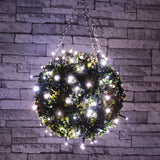 LYYT LED Battery Topiary Ball Light with 120 cool white LEDs wrapped around a green foliage sphere, hung by chain against a grey brick wall.