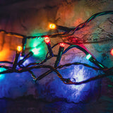 LYYT 120 LED battery topiary ball string light with multicoloured red, green, blue and yellow bulbs on black cable, draped across a stone wall outdoors.