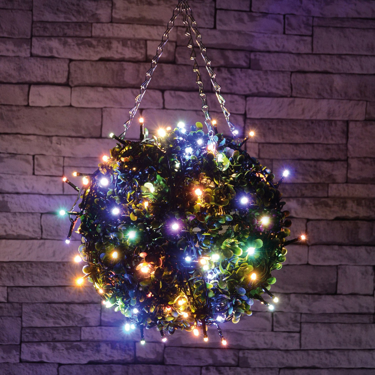 LYYT 120 LED battery topiary ball light with multicoloured LEDs on black cable wrapped around a green foliage ball, hung against a stone wall.
