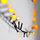 Close-up of LYYT amber LED string lights on a dark cable, with glowing bokeh dots from the 45m reel filling the soft grey background.