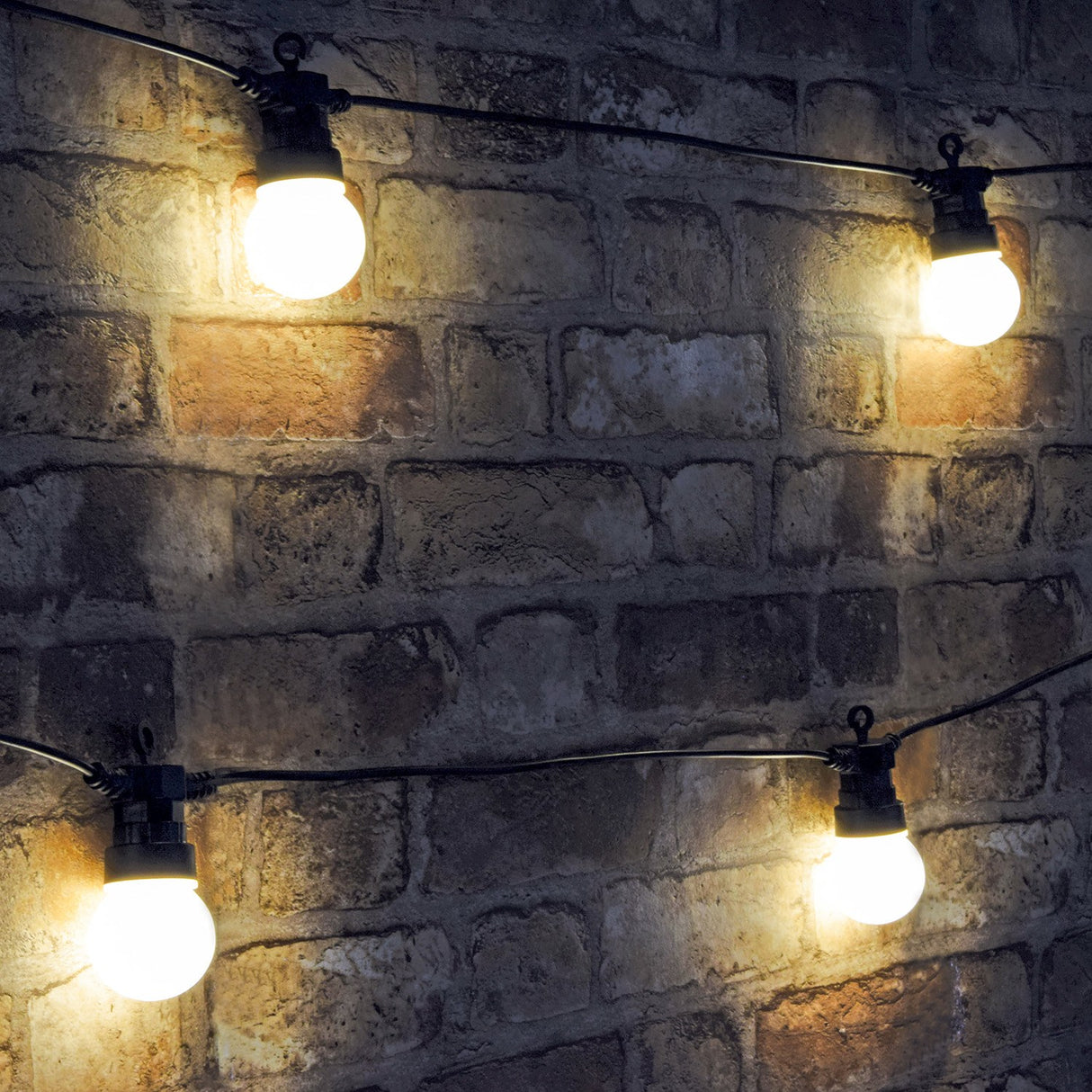 LYYT festoon string lights by AVSL with warm white polycarbonate globes on black cable, shown lit against an exposed brick wall outdoors.