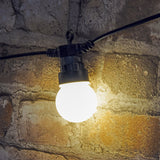 LYYT festoon string light with a warm white polycarbonate globe and black rubber cable, shown lit against a rustic stone brick wall.
