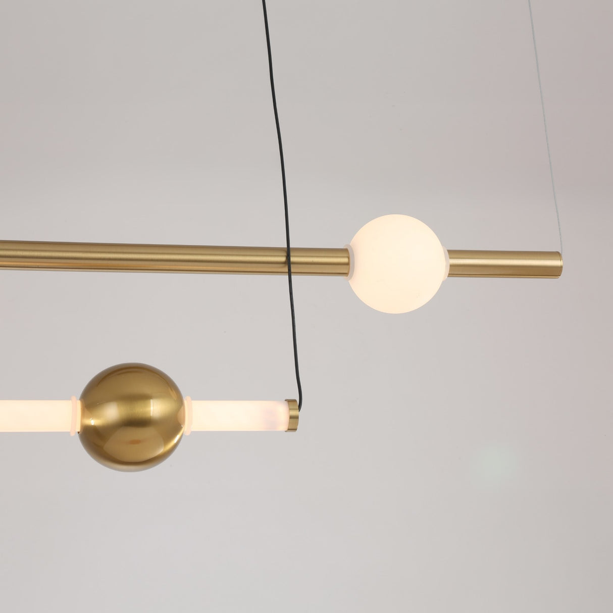 The Sottile LED Horizontal Suspension Light - Gold features a minimalist design with brass rods and spherical elements—one glowing white, one metallic—suspended by thin wires for a bold modern statement.