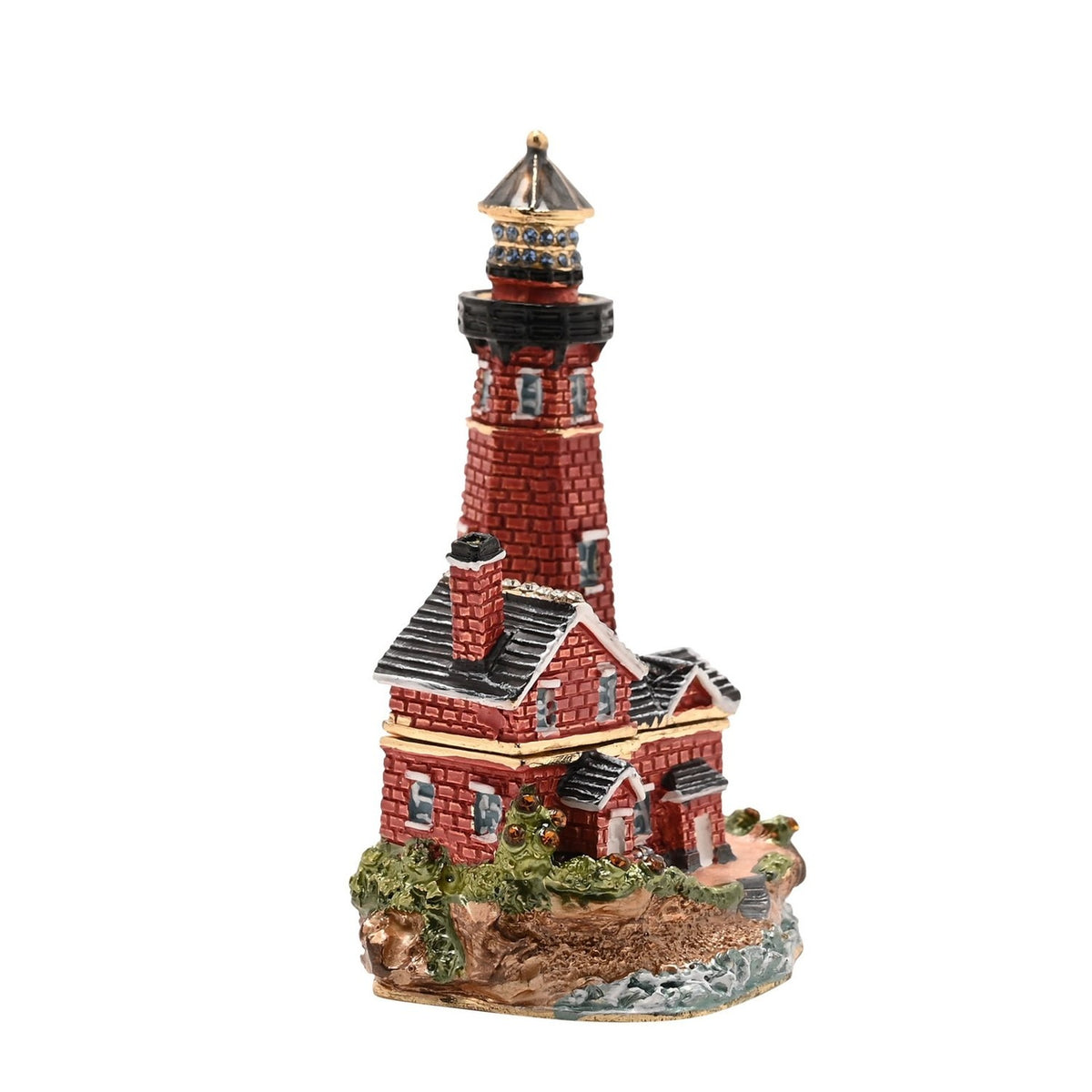 Painted metal trinket box shaped as a red brick lighthouse with gold bands, a blue-stone lantern gallery, and an attached grey-roofed keeper's cottage on a rocky base.