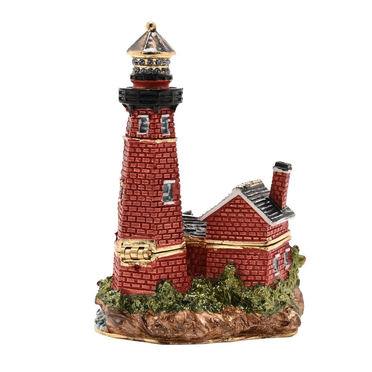 Painted metal trinket box shaped as a red brick lighthouse with gold bands and blue-stone lantern, beside a grey-roofed cottage on a rocky base, hinged lid, set against a plain white background.