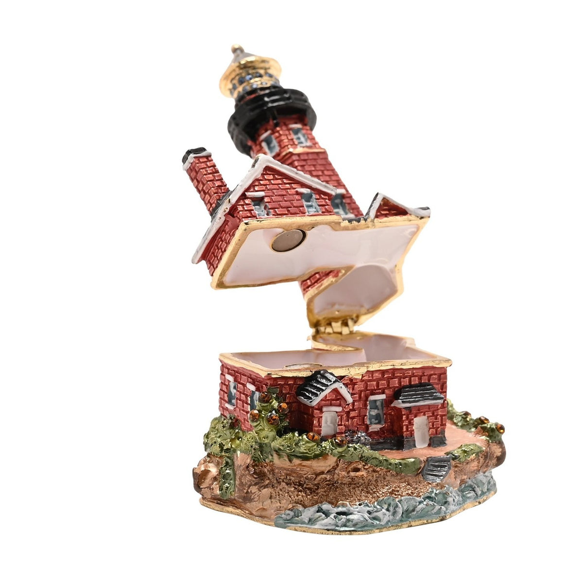 Painted metal trinket box shaped as a red brick lighthouse with gold bands and black lantern, hinged open above a keeper's cottage base on a rocky shore.