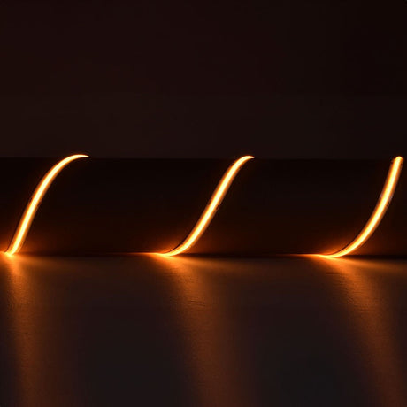 LYYT 24V COB LED strip light by AVSL curved in loops, glowing 2000K very warm amber-orange along a 5m flexible reel against a dark background.