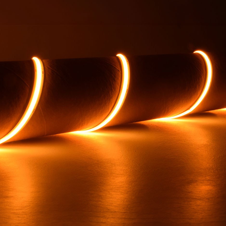 LYYT 24V COB LED strip light by AVSL coiled around a surface, emitting a very warm 2000K amber glow along its continuous flexible length.