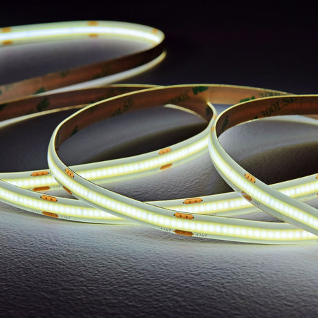 LYYT COB 24V LED tape by AVSL coiled in loops, emitting a continuous cool white glow with visible cut marks and adhesive backing on a dark surface.