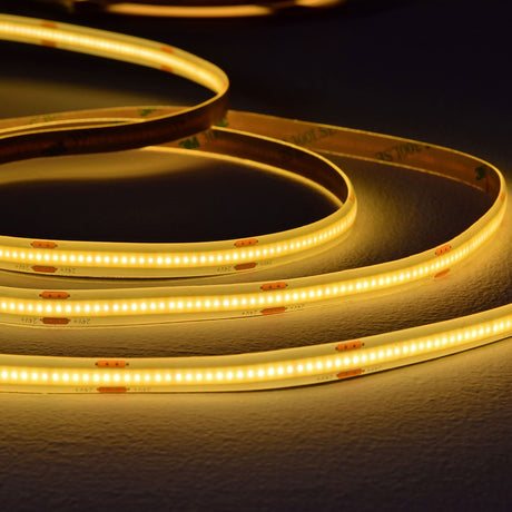 LYYT COB 24V LED tape by AVSL, coiled warm white lit strip on a textured surface showing dense LEDs and 24V cut-point markings along the reel.