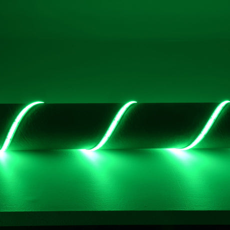 LYYT COB 24V RGB LED tape by AVSL installed along a shelf edge, lit in vivid green with a smooth dot-free line curving in waves against the wall.