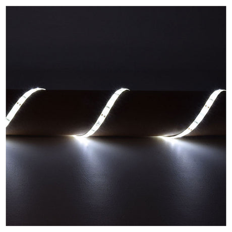 In a dimly lit room, the LYYT 12V SMD2835 Strip Light 5m - 6000K is installed along the top edge of the wall in a wavy pattern, illuminating the wall below with its soft, energy-efficient glow.