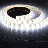 AVSL LYYT 24V RGBW LED strip light coiled on a dark wooden surface, illuminated in bright white with visible RGBW diodes and 3M adhesive backing.