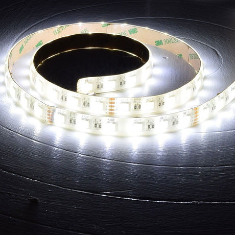 AVSL LYYT 24V RGBW LED strip light coiled on a dark wooden surface, illuminated in bright white with visible RGBW diodes and 3M adhesive backing.