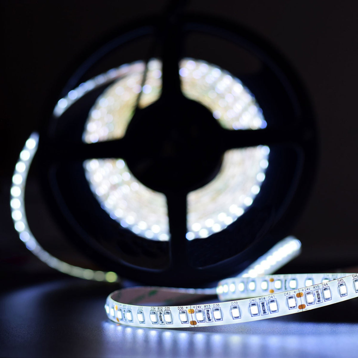 LYYT 24V LED strip light reel by AVSL illuminated in 6000K cool white, unspooled to show 2835 SMD LEDs on flexible white tape against a dark background.